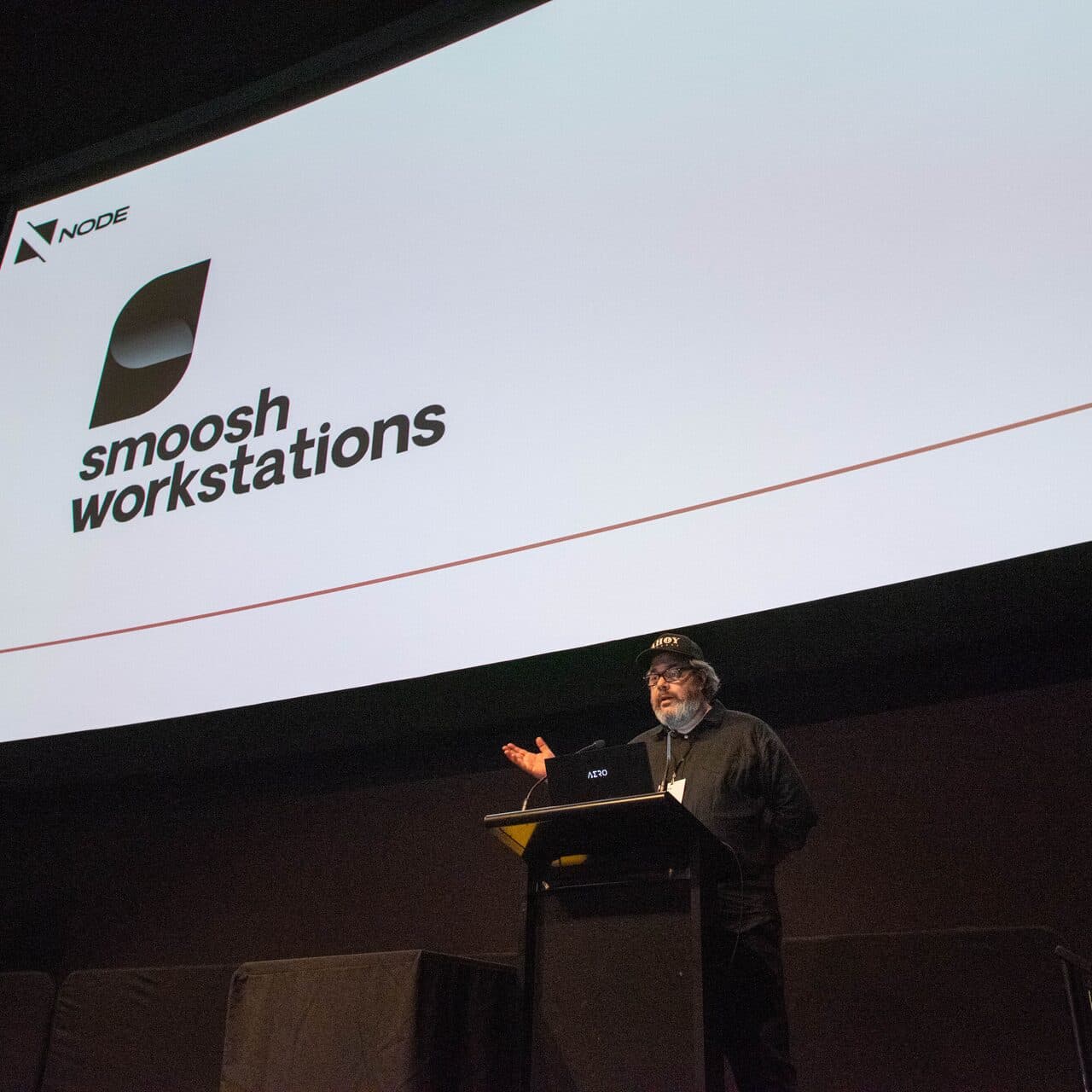 A speaker on stage at Node Fest 2022 in front of the Smoosh Workstations sponsor slide